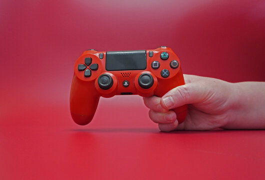 Red DualShock 4 gamepad in hand on a red background. PS4 controller, close-up, studio shooting.