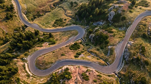 Aerial perspective of a curved mountain road snaking through a grassy highland landscape at sunset with mountain