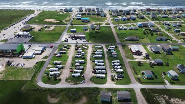Symmetrical motorhome rows anchor Surfside Beach RV Park grounds beside Fort Velasco Drive avenues. Dense coastal cottages border protective rock revetments across Brazoria County, Texas