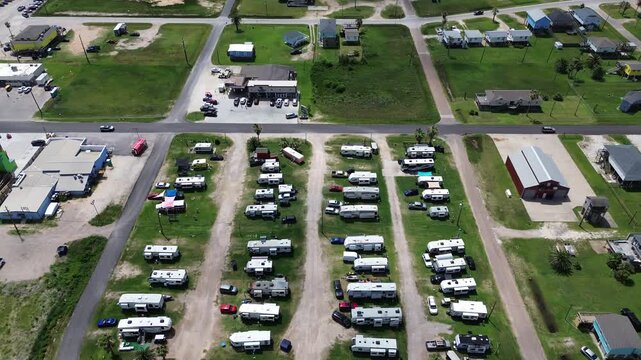 Parallel camper lanes border Fort Velasco Drive retail lots near Surfside Beach shoreline avenues. White recreational vehicles occupy manicured grassy sites across Brazoria County, Texas