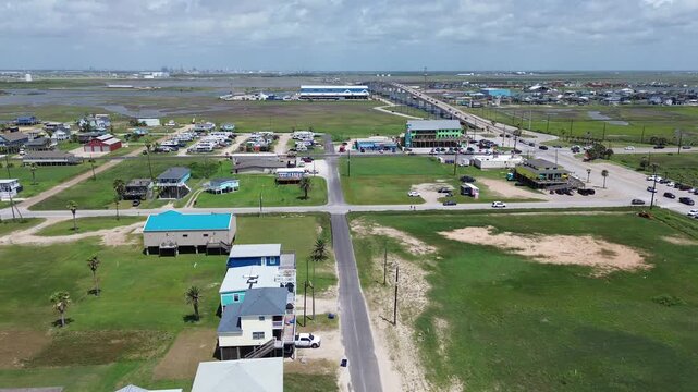 Elevated residential stilt cottages flank Fort Velasco Drive near State Highway 332 bridge approaches. Distant tidal marshes frame coastal communities across Surfside Beach, Texas