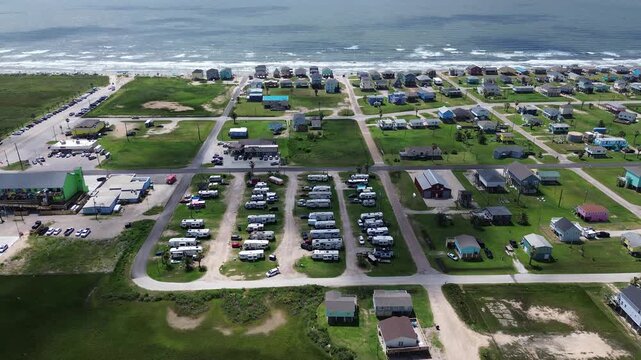 Grassy campground avenues extend past Fort Velasco Drive toward Follet's Island seaside properties. Raised stilt dwellings overlook rolling whitecaps across Surfside Beach, Texas