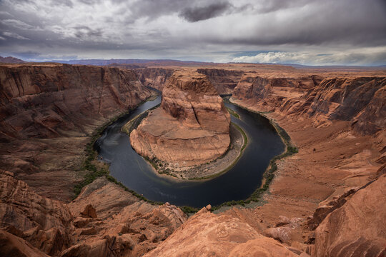 Aerial view of Horseshoe Bend, a dramatic meander of the Colorado River carved into deep red sandstone canyon walls under a cloudy sky in Coconino County, Arizona, United States.