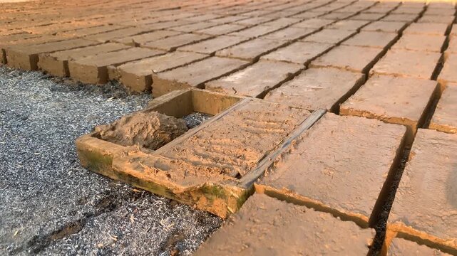 Close-up of a worker shaping and pressing wet clay inside a rectangular mold during traditional handmade brick production