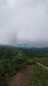 Vertical video. Aerial Flight Along Mountain Road Above Lake Batur, Tropical Forest and Low Clouds in Bali