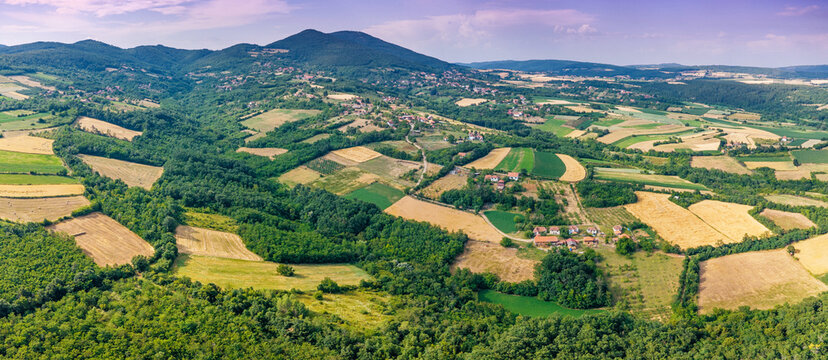 Aerial panoramic view of colorful patchwork farmland, orchards, and forested hills stretching to distant mountains. Rural landscape concept.