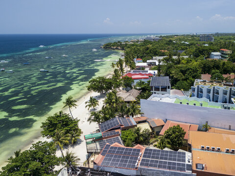 Aerial view of Alona Beach with turquoise waters, white sand, boats, and solar panels on rooftops in Panglao, Bohol, Philippines.