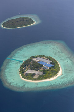 Aerial view of a tropical island with lush vegetation and white sandy beaches surrounded by turquoise coral reefs in the deep blue ocean in Baa Atoll, Baa Atoll, Maldives.