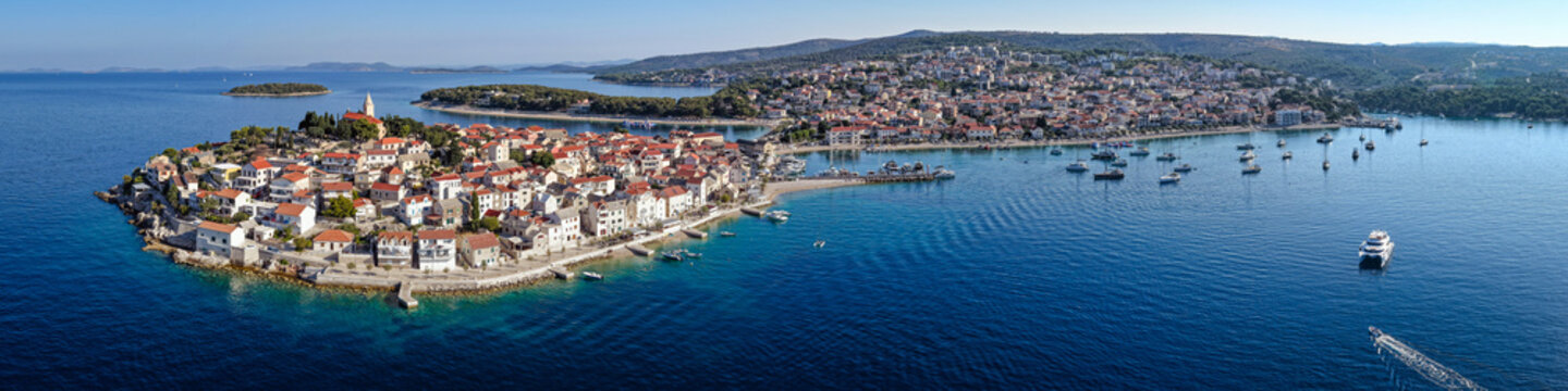 Scenic aerial panorama of historic Primosten old town peninsula with red tile roofs, church and boats floating in turquoise Adriatic Sea in Croatia