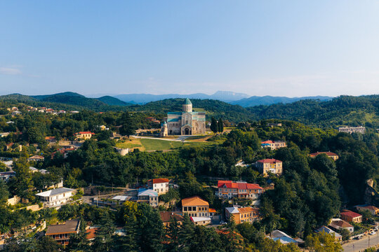 Aerial view of Bagrati Cathedral surrounded by lush green hills and residential houses with red roofs in Kutaisi, Imereti, Georgia.