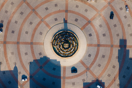 Aerial view of the Colchis Fountain surrounded by a circular paved square with geometric patterns and parked cars in Kutaisi, Imereti, Georgia.