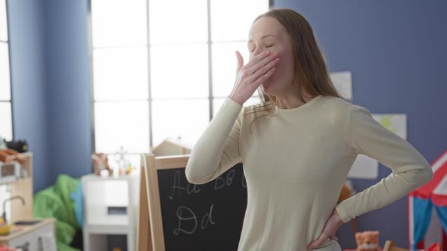 Woman standing with hands on hips and one hand covering her mouth beside a chalkboard in a classroom building; frustration.