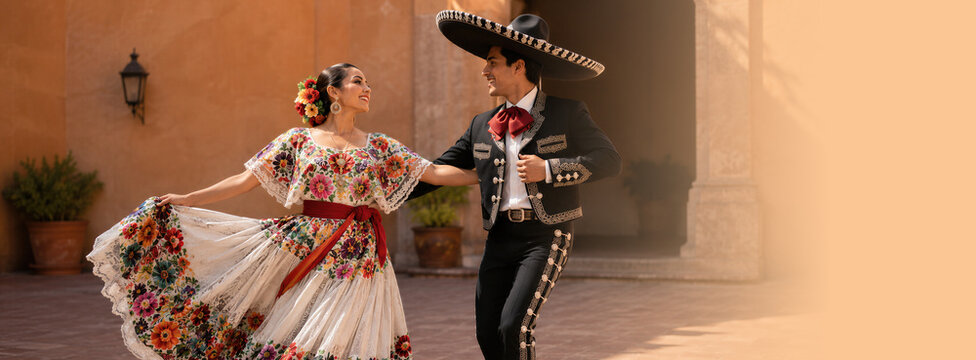 Woman and man dancing in traditional Mexican folkloric costume outdoors. Couple celebrating National Hispanic Heritage Month in embroidered dress and charro suit with sombrero. Banner with copy space