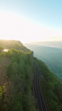 Vertical video. Smooth Cinematic Aerial Flight Along Coastal Cliffs And Scenic Road At Pantai Tanah Barak, Wide Angle Sunrise View Of Tropical Shoreline And Golden Horizon, Travel And Exploration