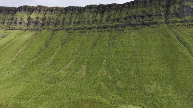 Detailed aerial drone footage of the rocky cliff face and eroded green slopes of Benbulben, County Sligo, Ireland.
