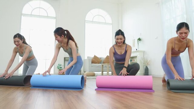 Group four Asian women each laid out their yoga mats, preparing yoga session focused on breath control and meditation aiming improve flexibility muscle strength balance and relaxation in the hall.