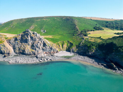 Aerial view of Valley of Rocks with dramatic rock formations, green grassy slopes, and a pebble beach meeting the turquoise sea in Lynton, England, United Kingdom.