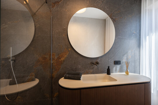 Bathroom vanity photographed with frameless shower glass and handheld fixture occupying the left side, beneath subdued indirect ceiling illumination.