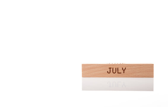 Wooden cube with engraved word JULY on white background with soft reflection. Concept of month, schedule, calendar, planning and time management.