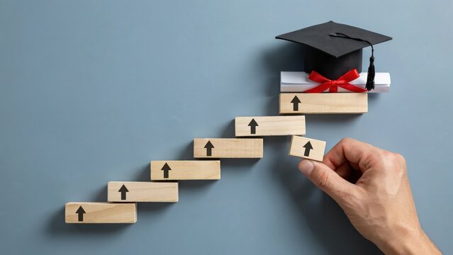 A hand placing a wooden block on stairs toward a graduation cap with a diploma. This image depicts academic success and professional educational attainment.