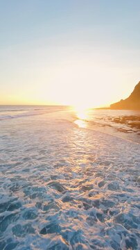 Vertical video. Chasing Shorebreak Toward Sunset at Nyang Nyang Beach, Dynamic Flight Just Above Ocean Foam Along Bali Coastline