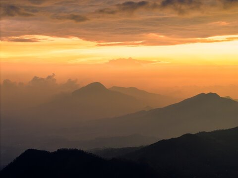 Aerial view of the mountainous landscape of Telaga Dringo at sunset with golden light illuminating the peaks and layers of hills in Indonesia.