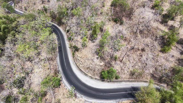 Slow motion bird's eye view from a drone looking straight down at a zig zag serpentine street in the hills. The empty paved pathway crosses through arid wilderness and sparse trees.