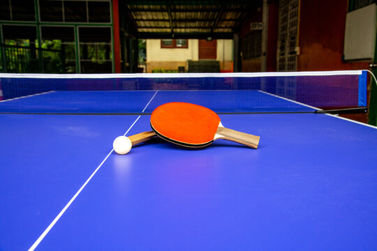 Table tennis paddle with white ball placed on blue ping pong table