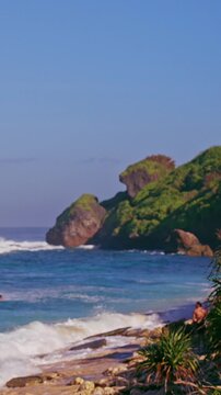 Vertical video. Rocky Coastline With Ocean Waves And Tropical Vegetation Under Clear Sky, Scenic Nature Landscape, Travel And Coastal Adventure