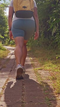 Vertical video. Young Female Traveler Walking Along Tropical Path Surrounded by Lush Greenery, Low Angle View Showing Active Exploration and Outdoor Adventure