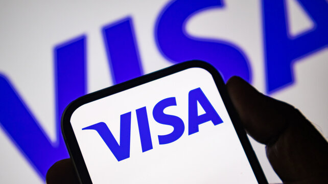 Person holding smartphone displaying blue visa logo on white screen in close up.
