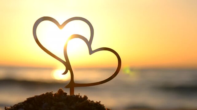 Two black outlines of heart at dawn sunset on sky on seashore. Stick contours in shape of heart in sand on background of setting and rising sun on seashore. Concept Love infatuation Valentine's Day
