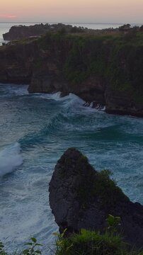 Vertical video. Powerful Ocean Waves Rolling Into Hidden Sandy Cove Beneath Rugged Coastal Cliffs in Slow Motion