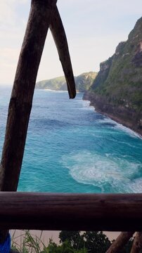 Vertical video. Determined Female Traveler Gripping Wooden Railings While Navigating the Dangerous Descent to Kelingking Beach in Slow Motion