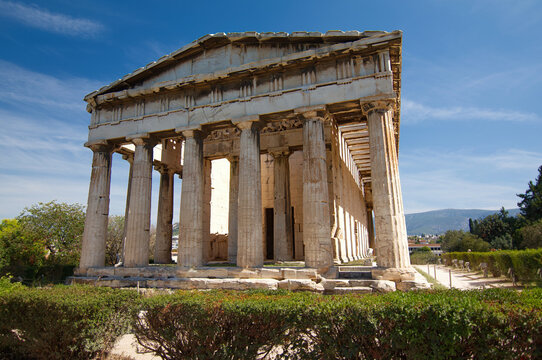 Front view of the ancient Doric Temple of Hephaestus above green hedges in Athens.