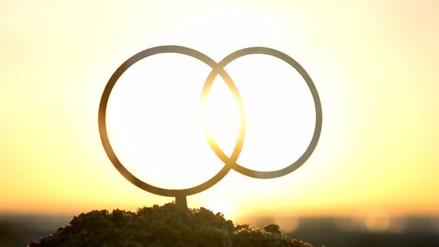 Black outlines wedding rings at dawn sunset on yellow sky. Stick contours in shape of wedding rings in sand on background of setting, rising sun. Concept wedding love romantic Valentine's Day holiday