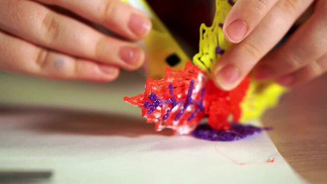 3D pen creation close up of boys hand shaping plastic flower with 3D printing pen device in 4K Ultra HD footage.
