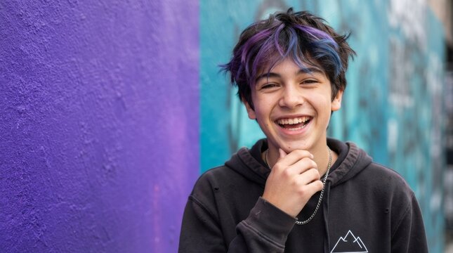 Portrait of happy teenage boy with purple curly hair laughing outdoors against graffiti wall. Joyful youth expression, positive emotion and generation z lifestyle concept