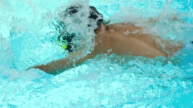 young boy swimming underwater in pool, practicing freestyle stroke with goggles and splashing water