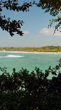 Vertical video. Ocean View Framed by Dense Tropical Vegetation Revealing Surfers and a Coastal Shoreline