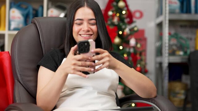 Happy hispanic woman smiling and texting on her mobile phone during the christmas season at a store