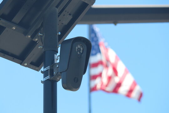 Flock camera monitoring a parking lot as an american flag waves in the background. 