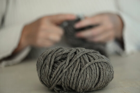 Close-up of a woman sitting at a table knitting with the ball of wool in the foreground