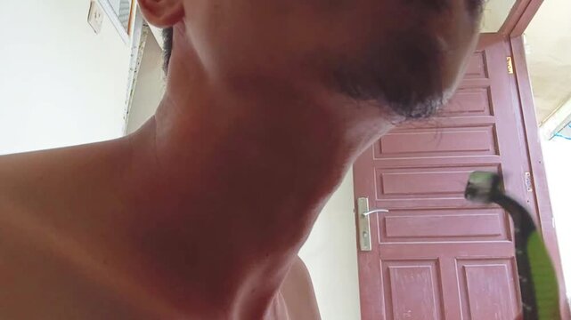 Man shaving facial hair with a manual razor at home, close-up grooming routine and personal hygiene activity.