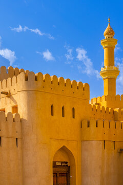 Nizwa Fort features a tall minaret and fortified walls under a clear sky in a historic setting