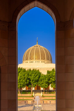 View of the dome and entrance of Sultan Qaboos Grand Mosque framed by an arch in Muscat, Oman during midday