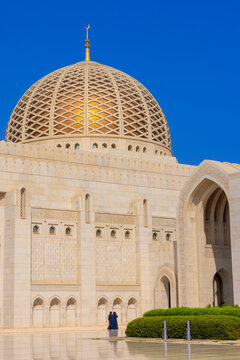 Muslim worshipper stands near the dome of Sultan Qaboos Grand Mosque in Muscat Oman during bright daylight hours