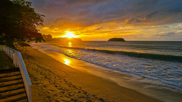 Sunset lights up La Toc beach, Saint Lucia with warm colors over the water and sand