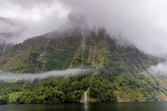 Views of waterfalls cascading down mountains in foggy Doubtful Sound during a cloudy day in Fjordland National Park