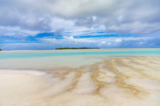Views of the uninhabited beach with clear water and sand patterns at Honeymoon Island in the Cook Islands on a cloudy day